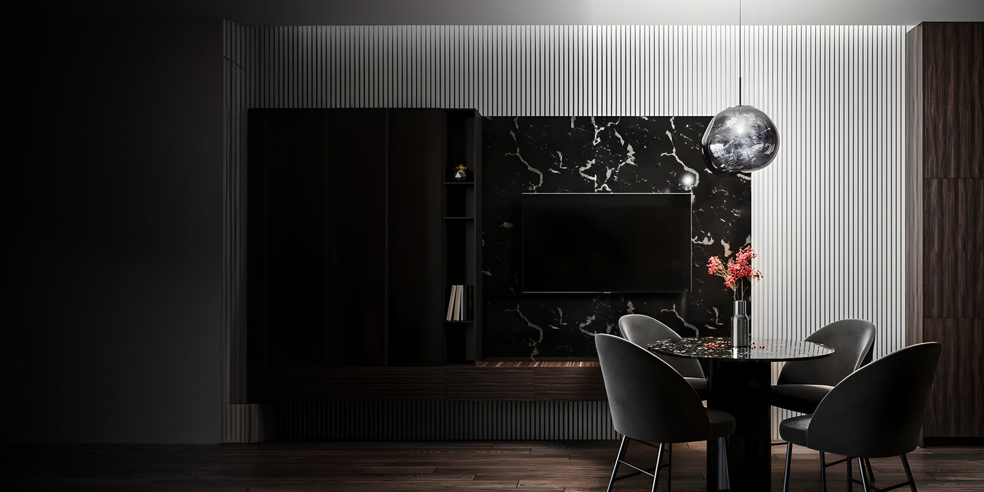 A modern, dimly lit dining area featuring a round black table with four dark chairs. A spherical pendant light hangs overhead. The wall has a black marble section with a TV and a single vase with red flowers on the table for decoration.