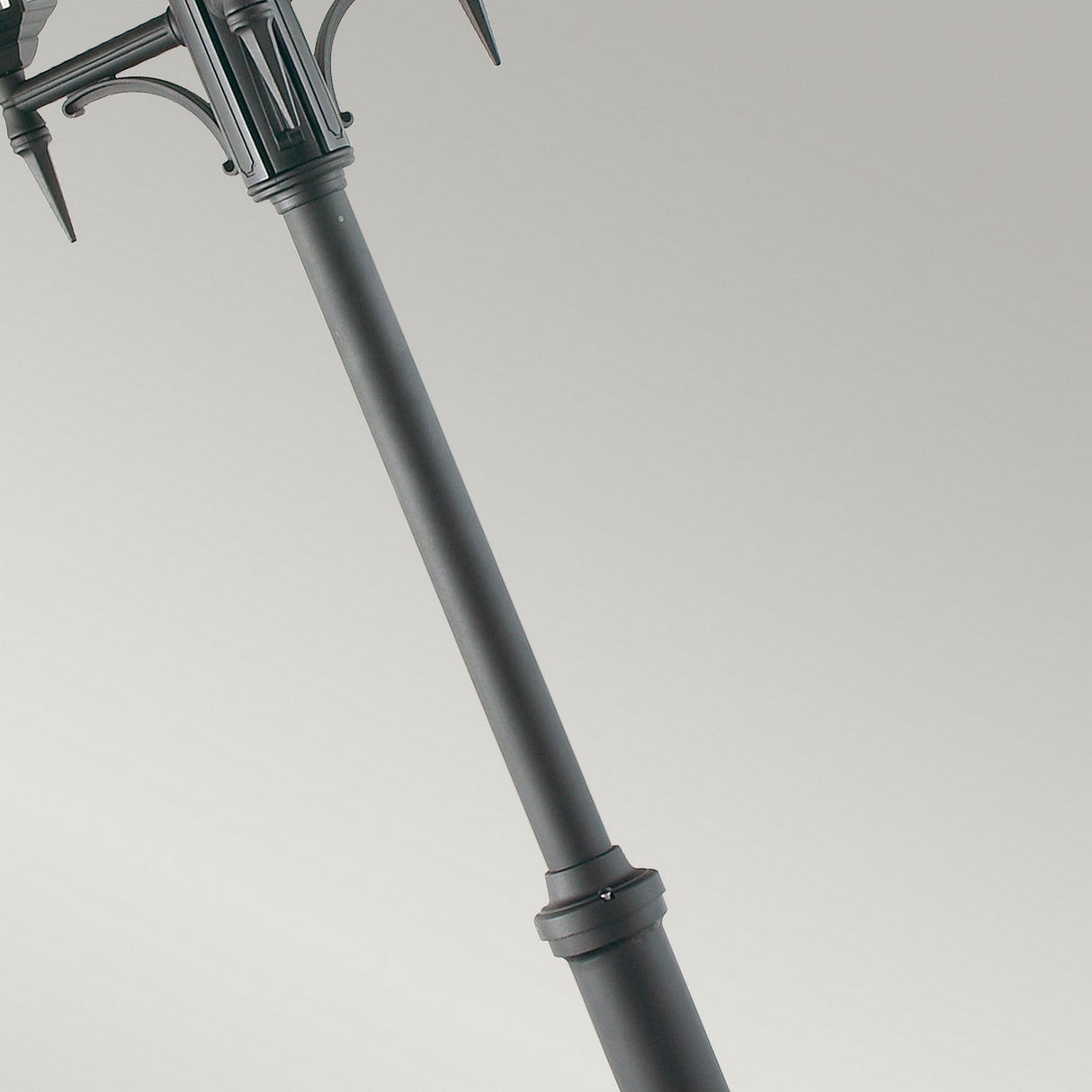 A sleek and modern black Valencia 3 Light Triple Head Lamp Post stands with a slight angle against a light gray background. Its upper section is adorned with decorative, curved elements, adding an elegant touch to outdoor lighting.