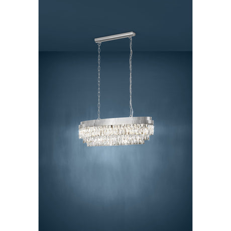 Valparaiso 10 light linear pendant with oval chrome frame and tiered faceted clear glass drops, hung from a ceiling bar on chains against a dark blue wall.