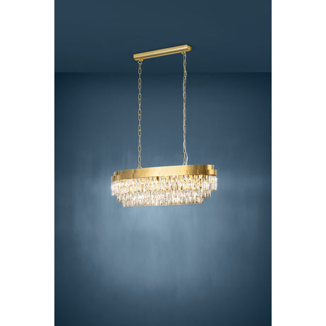 Valparaiso linear pendant light with an oval gold steel frame and tiered faceted clear glass drops, hung on gold chains from a slim ceiling bar, against a dark blue background.
