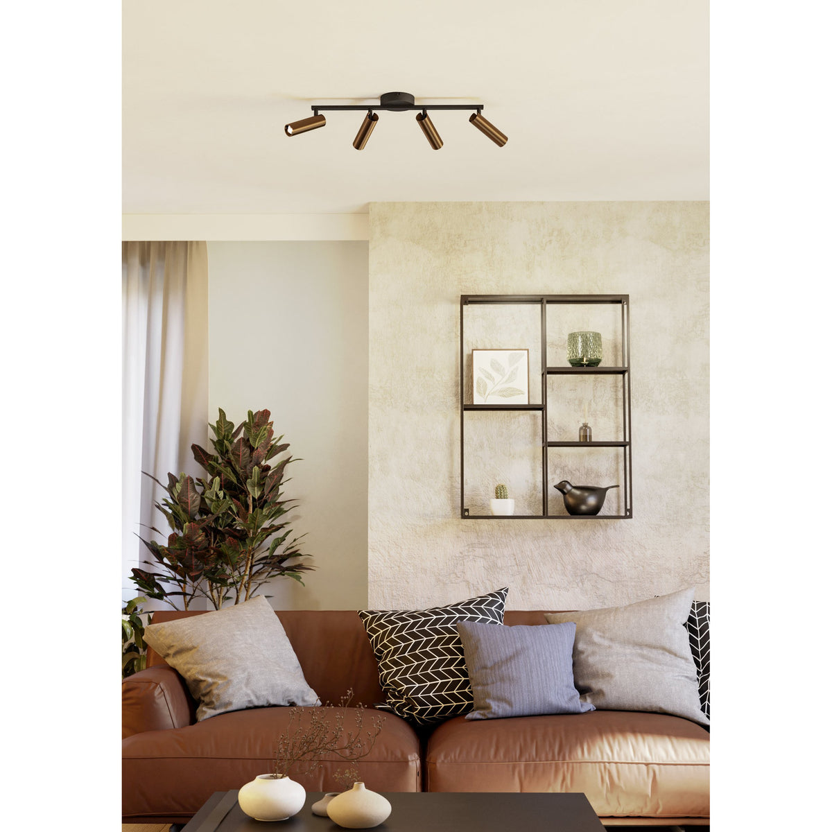 Valproto LED 4 Light Spotlight Bar in black steel with bronze cylindrical heads, mounted on a living room ceiling above a sofa and wall shelf.