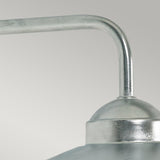 Close-up of the Vansbro Outdoor 1 Light Wall Lantern in silver, featuring a curved arm and dome-shaped shade in an industrial metallic style. Its brushed finish resembles galvanized steel, set against a simple light gray backdrop.