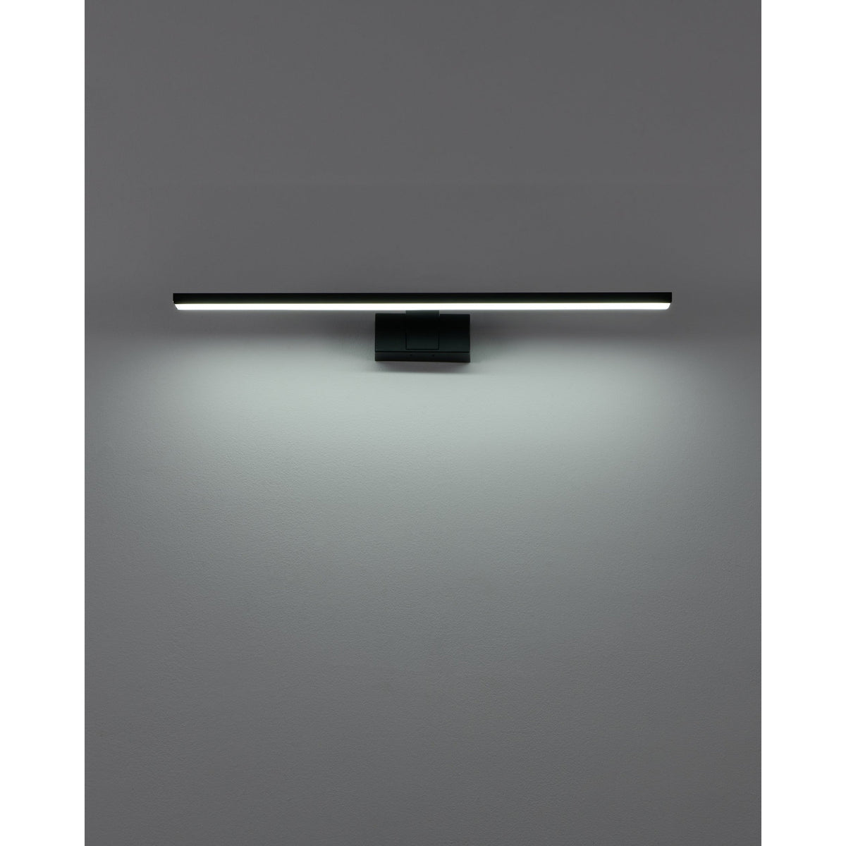 Varette LED Bathroom Mirror Light 60cm in black, a slim horizontal bar on a rectangular wall mount, illuminated above a grey wall with downward light spread.