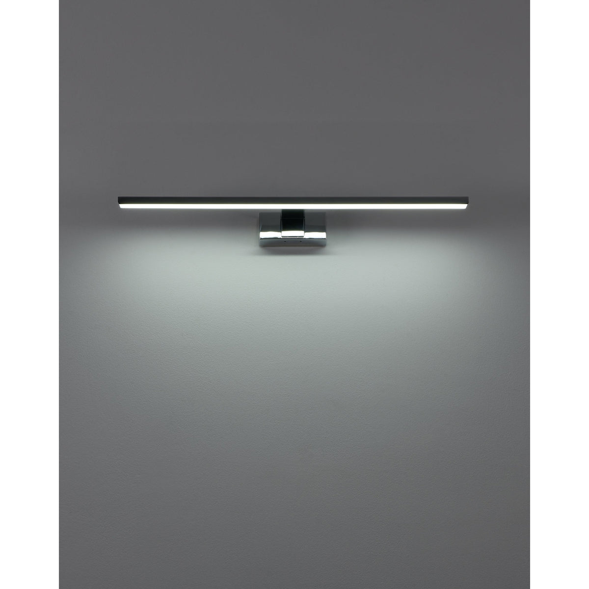 Varette 60cm LED bathroom mirror light in chrome, slim horizontal bar on a central wall bracket, illuminated with a soft downward glow against a plain grey wall.
