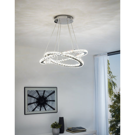 Varrazo Clear Glass Pendant Light in chrome, two interlocking rings with faceted glass hanging at an angle from a round canopy, shown above a console table in a living room.