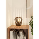Varvessa Table Lamp in bronze, a rounded steel cage-shade lamp with E27 bulb, shown on a wooden shelf beside stacked books in a living room setting.