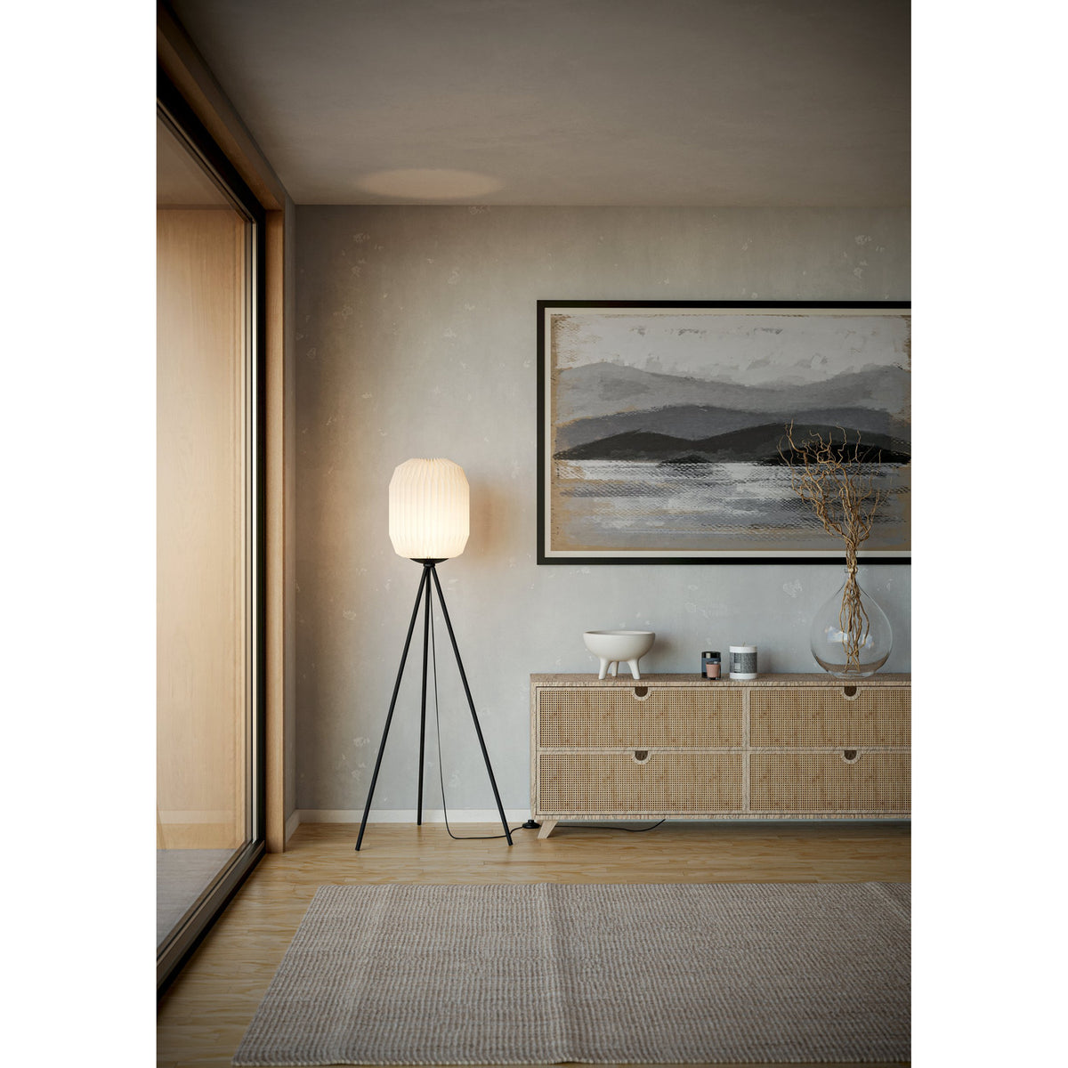 Vavanne Floor Lamp with pleated white paper lantern shade on a black tripod steel base, shown lit beside a sideboard in a living room.