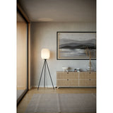 Vavanne Floor Lamp with pleated white paper lantern shade on a black tripod steel base, shown lit beside a sideboard in a living room.