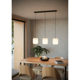 Vavanne Paper Linear Pendant Light featuring three white pleated paper lantern shades on a black steel ceiling bar, shown above a wooden dining table in a neutral-toned room.