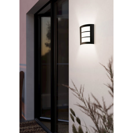 Velbessa Outdoor Wall Light in black, with a curved steel frame and three white plastic diffuser panels, mounted beside a glazed entrance door, illuminating the wall above and below.
