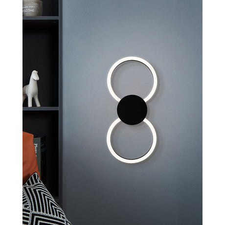 Venticello 1 LED Flush Ceiling Light in black, shown wall-mounted as two illuminated rings joined by a round disc, used as a hallway wall light beside a dark shelving unit.