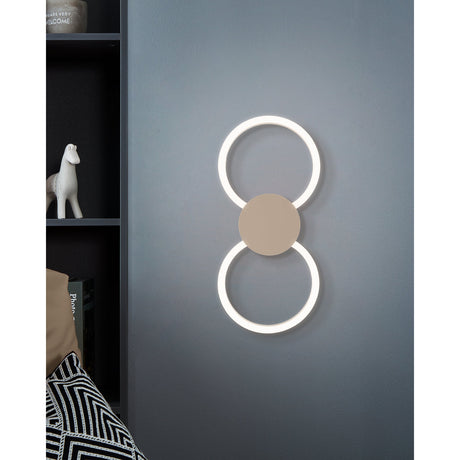 Venticello 1 LED wall light in Sand finish, two illuminated white plastic rings joined by a round aluminium centre disc, shown mounted on a grey bedroom wall.