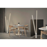 A modern dining area with round tables, wooden chairs, and a Vertical Dimmable LED Floor Lamp 60W 3000K - White offering soft white light. A small black divider separates the space, complementing the minimalist decor and neutral tones.
