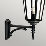 The Valencia Outdoor Large 1 Light Up Lantern - Black is a die-cast aluminum, wall-mounted fixture with a transparent glass enclosure that reveals the visible light bulb inside. Featuring an IP54 rating, its decorative arm elegantly stands out against a plain gray background.