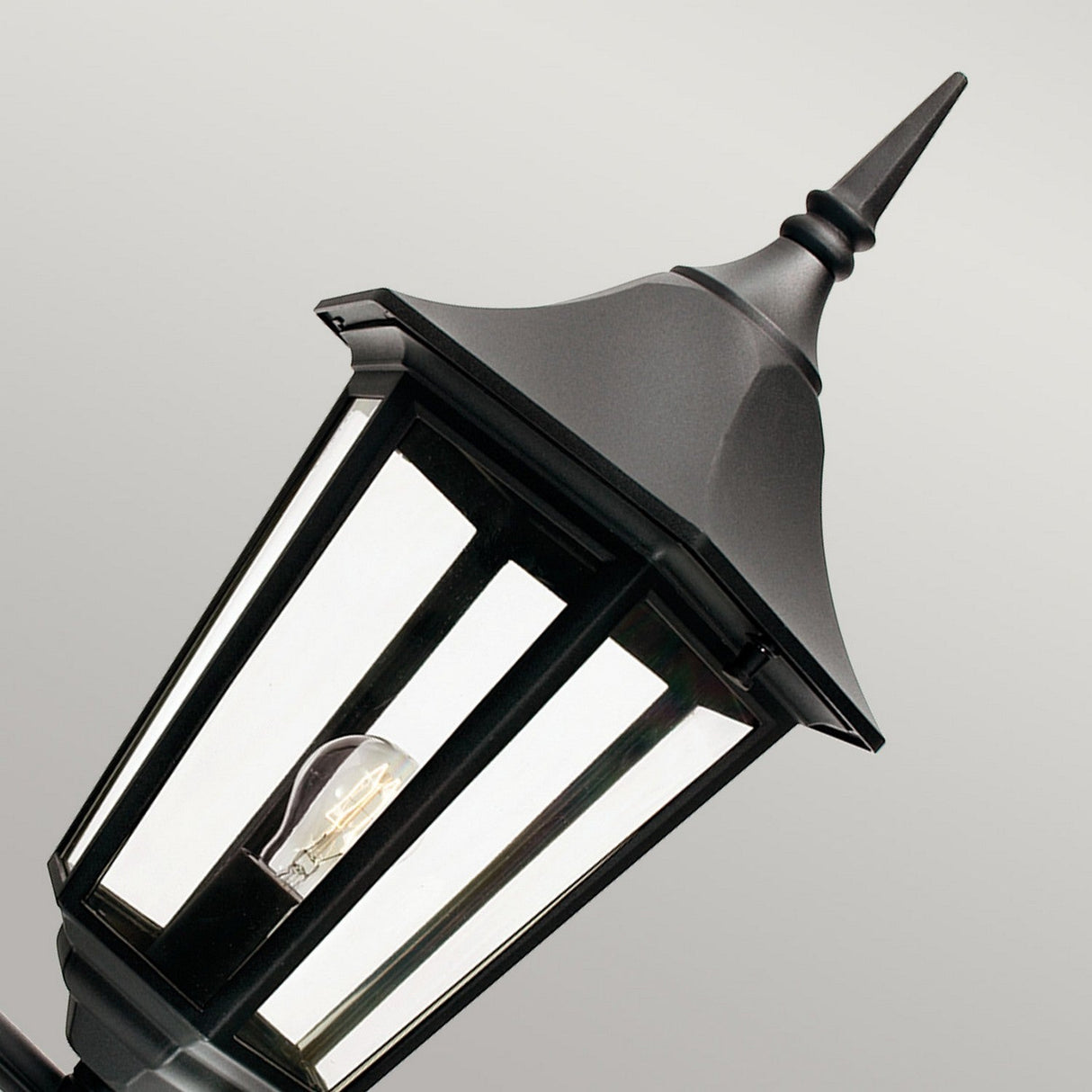 Introducing the Valencia Outdoor Large 1 Light Up Lantern in classic black, expertly crafted from die-cast aluminium with a pointed top design. It features clear glass panels and a visible bulb inside, all set against a plain gray backdrop. With an IP54 rating, this lantern guarantees durability and weather resistance.