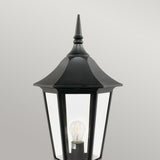 The Valencia Large 1 Light Pedestal - Black is a traditional-style outdoor lantern made from die-cast aluminum. It features a pointed top and showcases a clear glass enclosure that reveals the bulb inside, making it an excellent choice for outdoor lighting. The backdrop is a simple light gray.