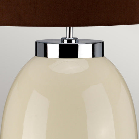 Close-up of the Victor 1 Light Small Table Lamp - Cream, featuring a glossy off-white ceramic base with chrome accents and a dark brown faux silk shade. The image emphasizes the upper part of the lamp, showcasing its sleek and modern design.