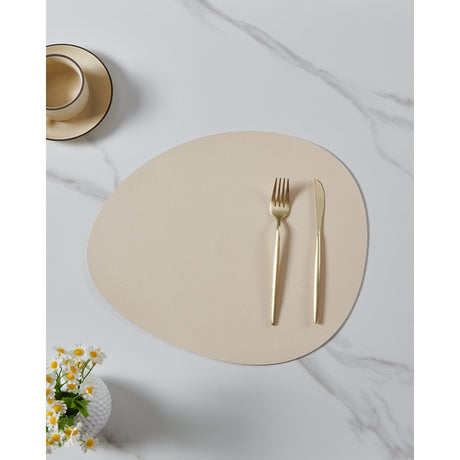 Vinanivao pebble-shaped placemat in cream white, shown with gold cutlery on a marble surface beside a cup and saucer and a small flower vase.
