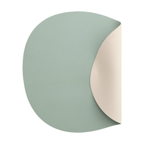 Vinanivao reversible pebble-shaped placemat in plastic with a fine grain texture, sage green on one side and cream white on the other, shown against a plain white background.