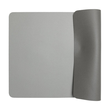 Vinanivao reversible rectangular placemat with rounded corners, pebbled leather-look finish, light grey on one side and dark grey on the other, shown partly rolled on a white background.