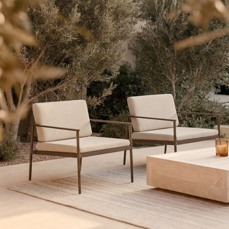 Vint Aluminium Garden Lounge Chairs with cream cushions and slim bronze-toned frames, shown outdoors on a patio beside olive trees and a wooden coffee table.