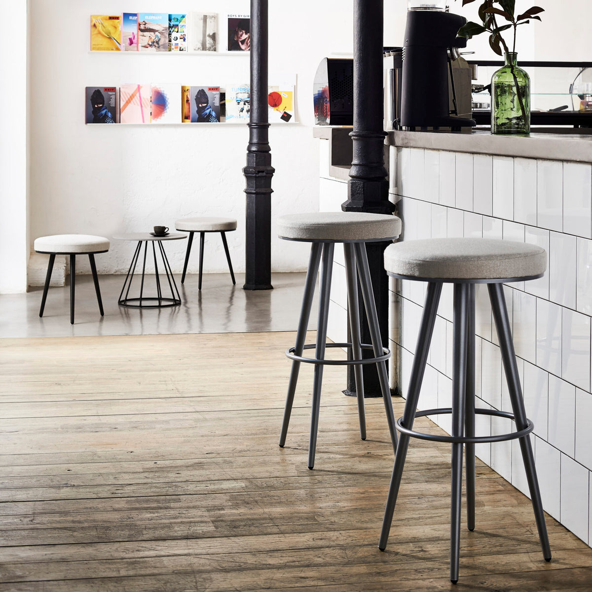 Vint Aluminium Outdoor Bar Stools with round beige seat cushions, slim tapered legs and ring footrests, shown in a café-style indoor setting.