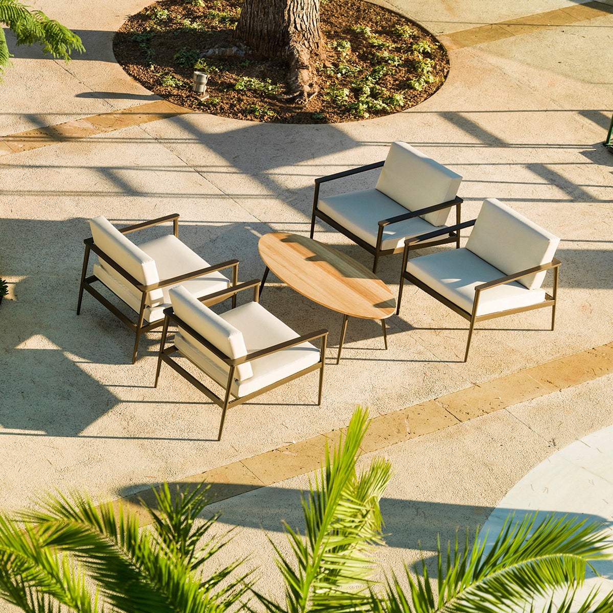 Vint Aluminium Oval Outdoor Coffee Table with wood-toned top and slim dark legs, set on a patio with white lounge chairs around it.