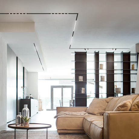 Viora 2m Recessed Magnetic Track in black, shown flush in a living room ceiling with integrated LED strip lighting above a sofa and glass shelving unit.