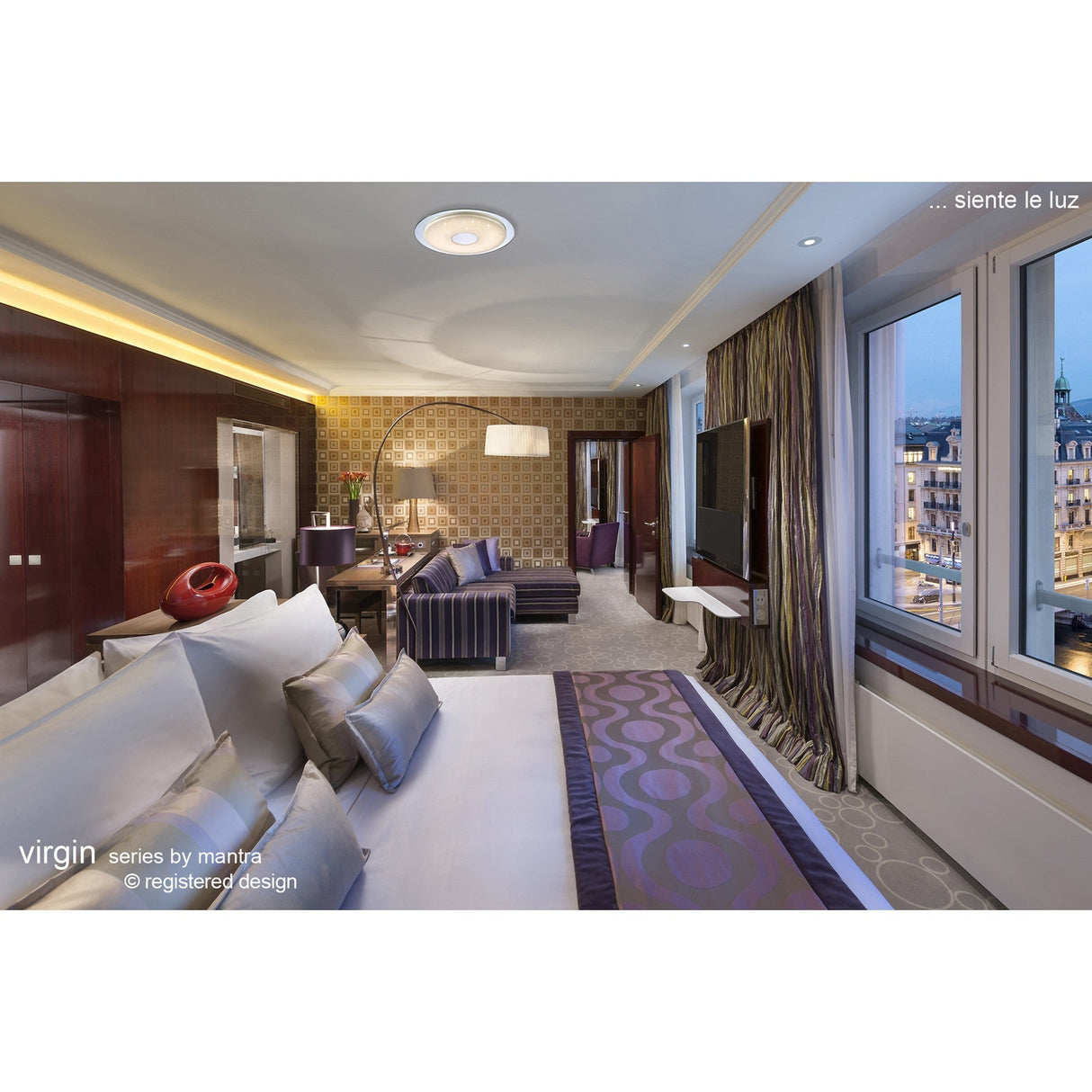 Mantra Virgin CCT dimmable LED flush ceiling light with silver ring and crystal-effect centre, shown in a contemporary hotel-style bedroom with city view.