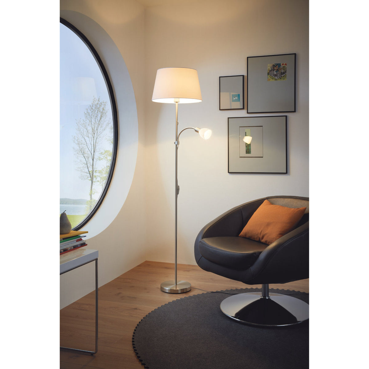 Vorbine mother and child floor lamp in satin nickel with a white fabric shade and gooseneck reading arm, shown beside a black armchair in a living room.