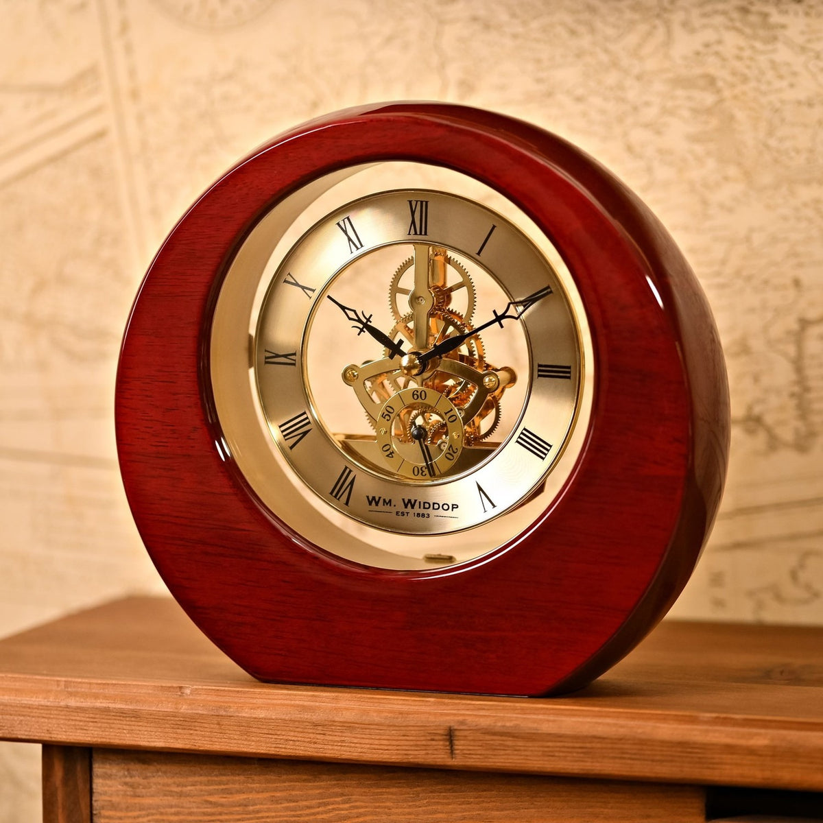 Round mantel clock in high-gloss mahogany piano wood with gold-tone dial, black Roman numerals, and an open skeleton movement showing gears, displayed on a wooden surface.