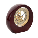 Round mantel clock in high-gloss mahogany wood case with open skeleton movement, gold-tone dial, black Roman numerals, and visible gears, set against a white background.