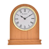 Arched oak mantel clock with rounded top and plinth base, featuring a white Roman numeral dial, gold-coloured bezel and black spade hands, shown on a plain white background.