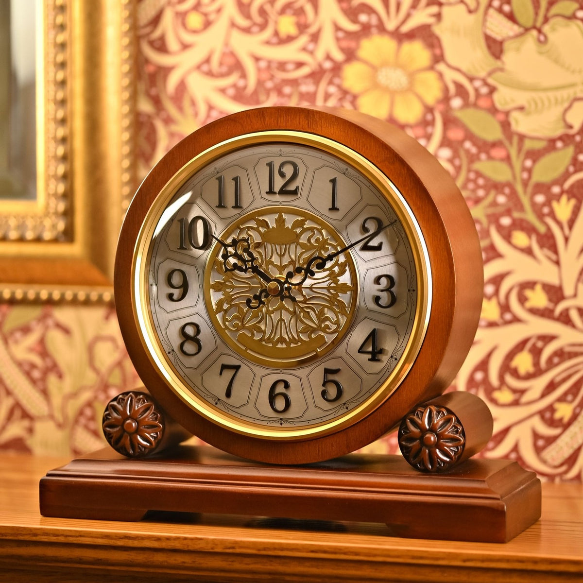Walnut-finish Westminster barrel mantel clock with gold-coloured bezel, silver-white dial, black Arabic numerals, ornate gold filigree centre, and scrolled hands on a decorative wooden base.
