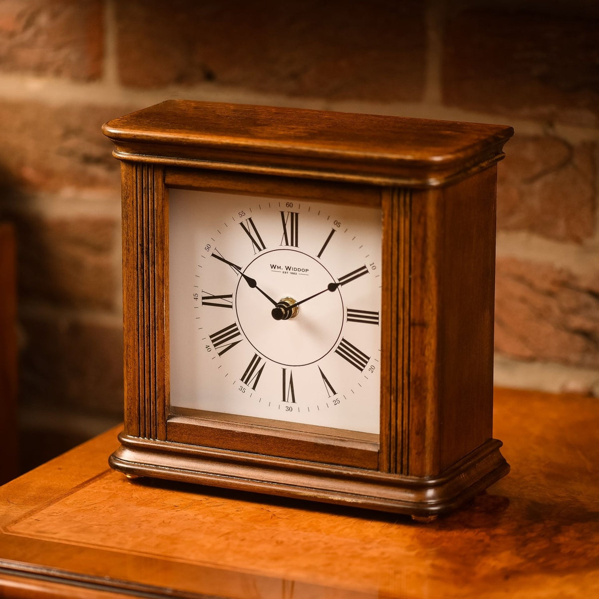 Square walnut effect Westminster chime mantel clock with white dial, black Roman numerals, spade hands, and fluted side columns, shown on a wooden surface.
