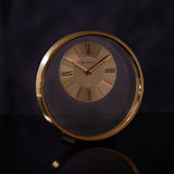 Round metal mantel clock with a slim gold ring frame and open centre, featuring a two-tone gold dial with black Roman numerals and slender gold hands.