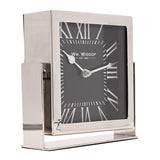 Square mantel clock with silver frame and stand, black dial, white Roman numerals and minute markers, shown at an angle on a plain white background.