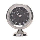 Round mantel alarm clock on a pedestal foot, with a silver casing, black dial, white Arabic numerals, and silver hands, shown on a plain white background.