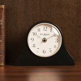 Napoleon arch mantel clock in black resin with matt finish, round white dial, silver rim, black Arabic numerals and slim silver hands, shown beside a leather-bound book.
