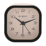 Rounded square metal alarm clock with black case and cream dial, bold black Arabic numerals, black hour, minute and alarm hands, on a plain white background.