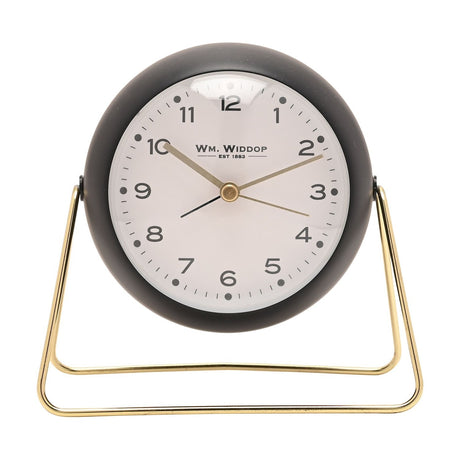 Medium Kent round metal alarm clock in matt black with a white dial, gold hands, and numbers one to twelve, set on a slim gold wire stand against a plain white background.