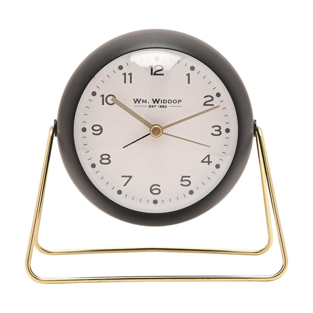 Medium Kent round metal alarm clock in matt black with a white dial, gold hands, and numbers one to twelve, set on a slim gold wire stand against a plain white background.