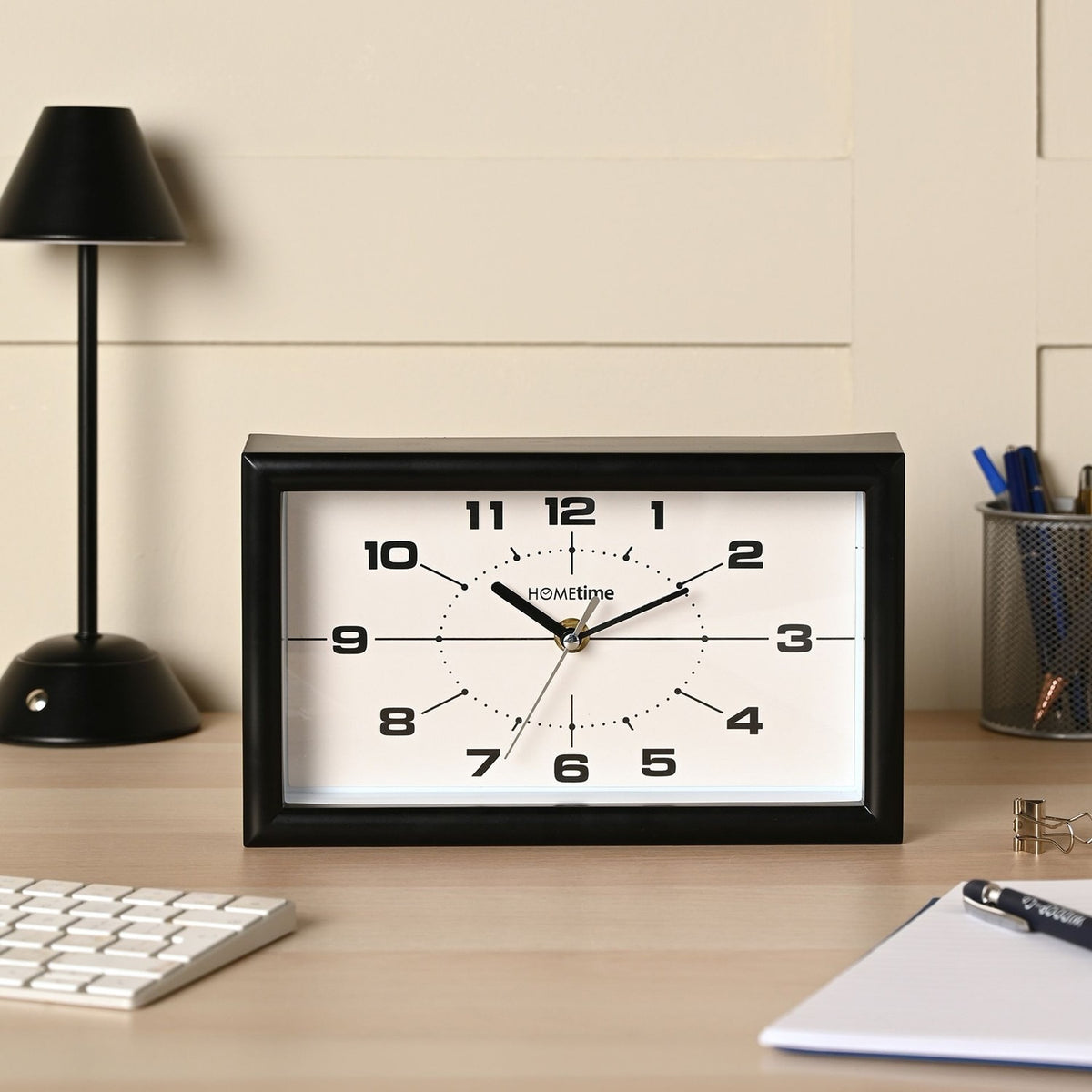 Modern rectangular mantel clock, 25cm, with black frame and white dial featuring bold numerals, shown on a desk beside a lamp and keyboard.