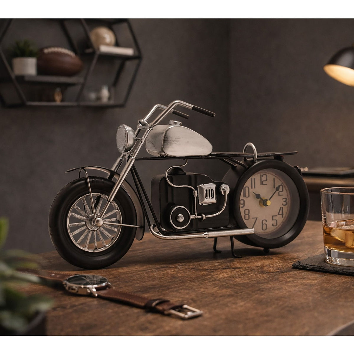 Motorbike-shaped metal mantel clock with black frame, seat and tyres, silver fuel tank, headlamp and spoked front wheel, round cream dial set as the rear wheel, displayed on a wooden desk.