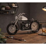 Motorbike-shaped metal mantel clock with black frame, seat and tyres, silver fuel tank, headlamp and spoked front wheel, round cream dial set as the rear wheel, displayed on a wooden desk.