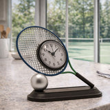 Tennis Racket and Ball Metal Mantel Clock in silver and black, with a blue-rimmed racket head framing a white clock face, leaning on a silver ball atop a black plinth, shown on a kitchen counter.