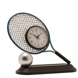 Silver tennis racket metal mantel clock with round white face, blue rim, green throat, and black handle resting on a silver ball atop a black plinth, white background.