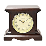 Square mantel clock in dark walnut finish with stepped moulded top and squared pillars, featuring a cream dial, black Roman numerals and gold-coloured rim, shown on a plain white background.
