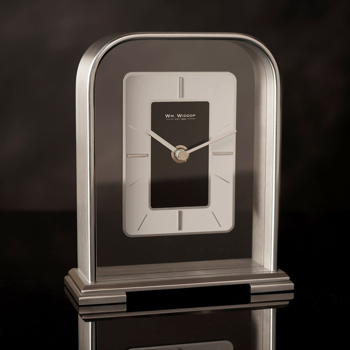 Arched portrait mantel clock in silver metallic finish with rectangular black centre dial, silver-grey surround, baton markers, and stepped base, set against a dark background.