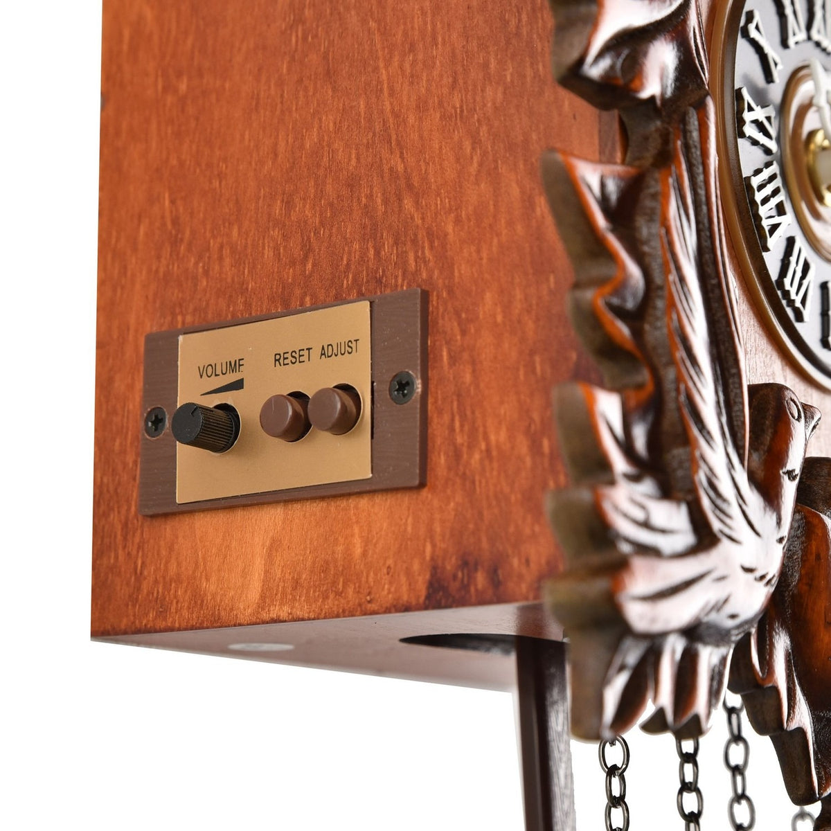 Close-up of the Pitched Roof Quartz Wooden Cuckoo Wall Clock in mahogany, showing the side control panel with volume dial and reset/adjust buttons beside the carved wood case and Roman numeral dial.